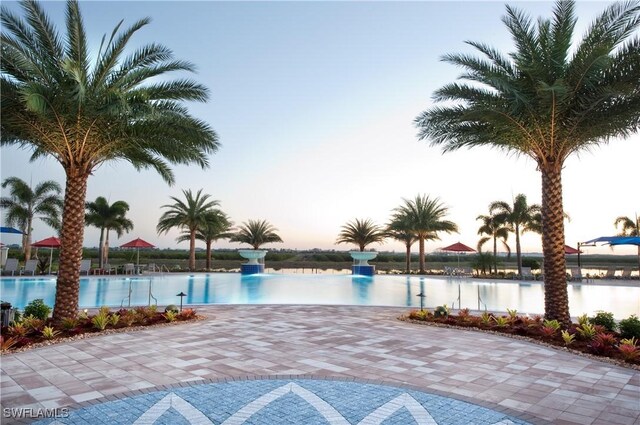 pool at dusk featuring a water view and a patio area