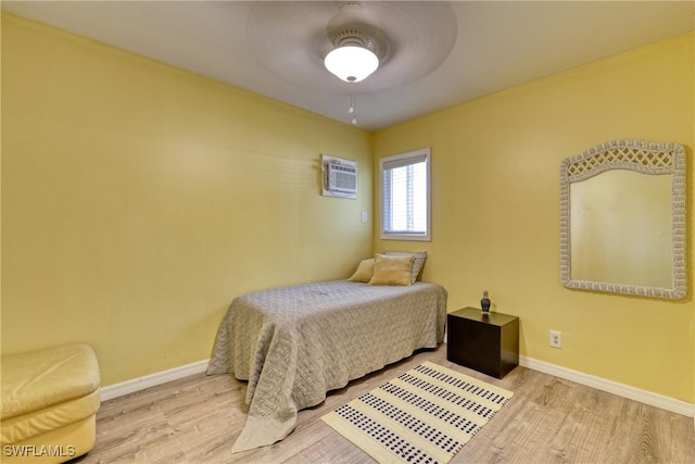 bedroom with ceiling fan, an AC wall unit, and light hardwood / wood-style flooring