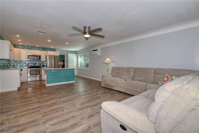 living room with sink, a wall unit AC, ornamental molding, ceiling fan, and light hardwood / wood-style flooring