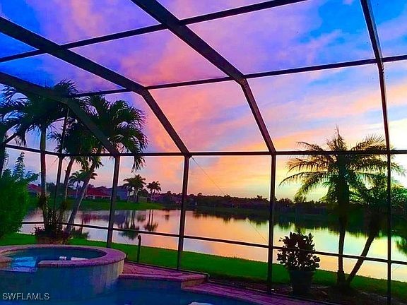 pool at dusk featuring a lanai, a water view, and an in ground hot tub