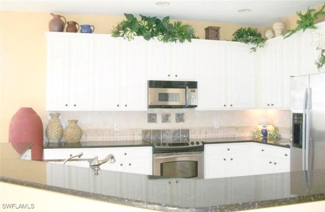 kitchen with appliances with stainless steel finishes, kitchen peninsula, dark stone counters, decorative backsplash, and white cabinetry