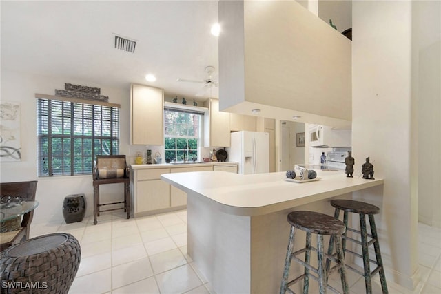 kitchen with ceiling fan, a kitchen breakfast bar, kitchen peninsula, white appliances, and light tile patterned flooring