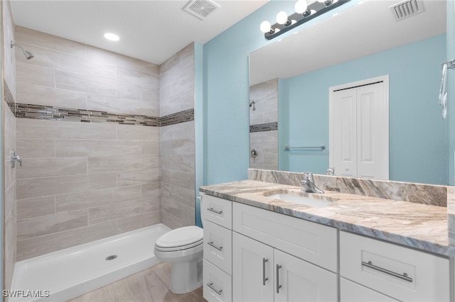 bathroom with tiled shower, hardwood / wood-style floors, vanity, and toilet