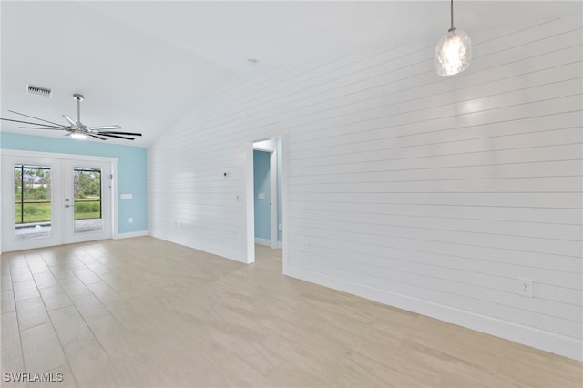 empty room with wood walls, french doors, light hardwood / wood-style flooring, vaulted ceiling, and ceiling fan