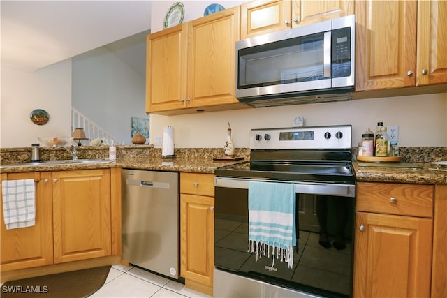 kitchen with dark stone countertops, sink, light tile patterned floors, and stainless steel appliances