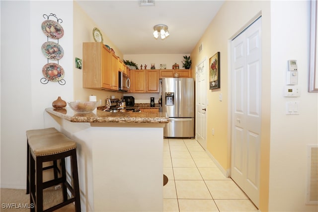 kitchen with light tile patterned floors, a breakfast bar area, kitchen peninsula, light stone countertops, and stainless steel appliances