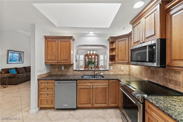 kitchen featuring sink, an inviting chandelier, backsplash, dark stone countertops, and appliances with stainless steel finishes