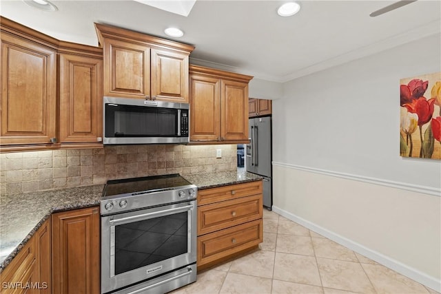 kitchen featuring dark stone counters, appliances with stainless steel finishes, brown cabinetry, and ornamental molding