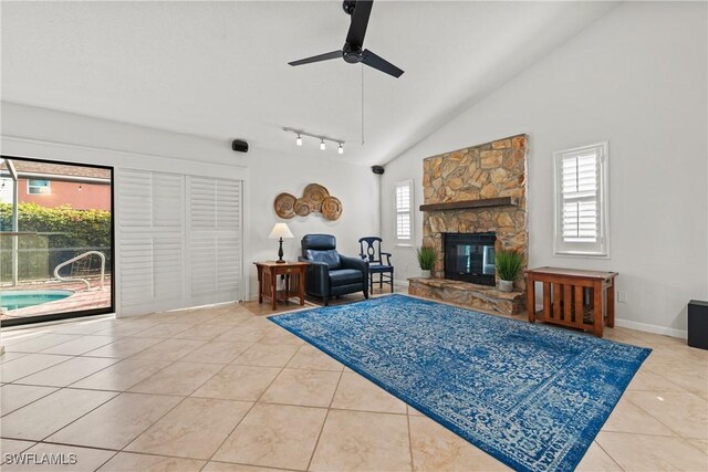 living room with track lighting, ceiling fan, light tile patterned floors, high vaulted ceiling, and a stone fireplace