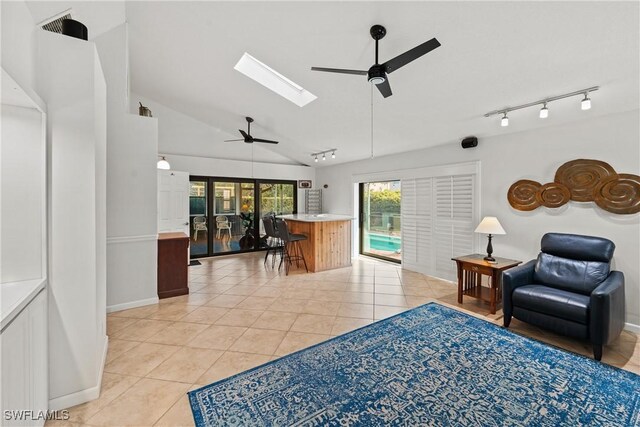 living area with a ceiling fan, track lighting, light tile patterned flooring, and lofted ceiling with skylight