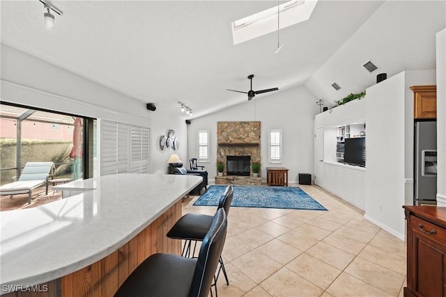 kitchen featuring a kitchen bar, stainless steel fridge, lofted ceiling with skylight, ceiling fan, and a fireplace