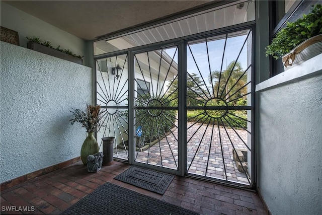 doorway with brick floor, baseboards, and a textured wall