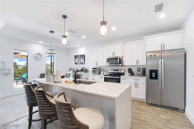 kitchen featuring appliances with stainless steel finishes, sink, pendant lighting, light hardwood / wood-style flooring, and white cabinetry