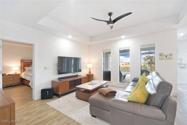 living room with ceiling fan, light wood-type flooring, and a tray ceiling