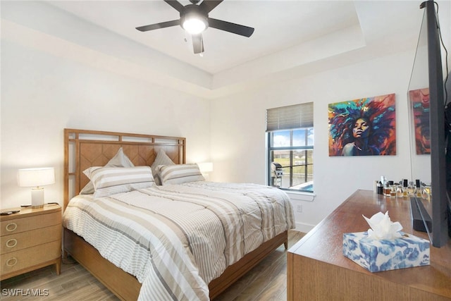 bedroom featuring hardwood / wood-style flooring, ceiling fan, and a raised ceiling