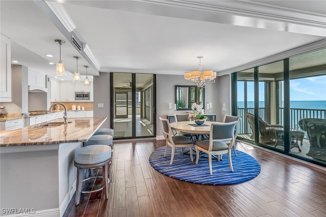 dining room with sink, a water view, ornamental molding, a chandelier, and dark wood-type flooring