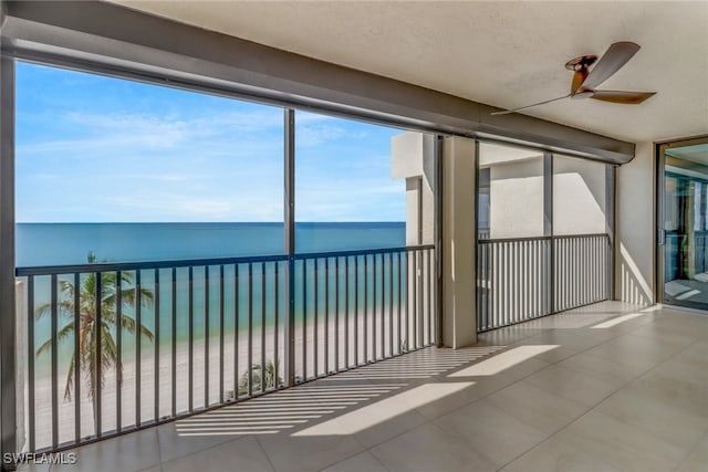 unfurnished sunroom with a beach view, a water view, and ceiling fan