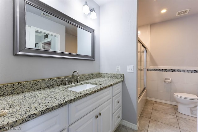 full bathroom with tile patterned flooring, combined bath / shower with glass door, toilet, vanity, and tile walls