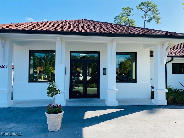 doorway to property with stucco siding, a porch, and a tiled roof