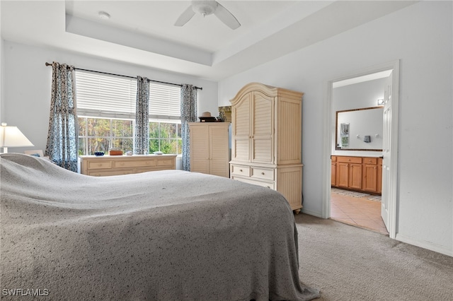 bedroom featuring ceiling fan, a raised ceiling, light carpet, and connected bathroom