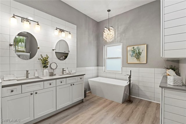 bathroom with tile walls, a tub to relax in, hardwood / wood-style flooring, vanity, and an inviting chandelier