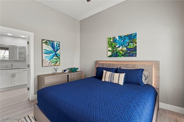 bedroom with ensuite bath, lofted ceiling, sink, and light hardwood / wood-style flooring