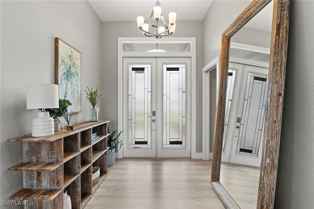 foyer entrance featuring light hardwood / wood-style flooring, a notable chandelier, and french doors