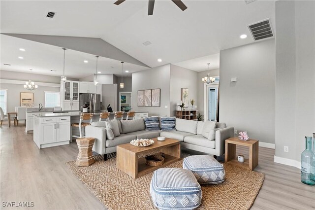 living room featuring ceiling fan with notable chandelier, light wood-type flooring, lofted ceiling, and sink