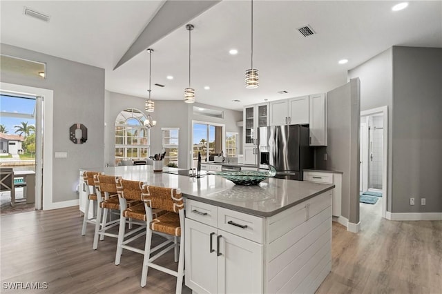 kitchen featuring white cabinetry, stainless steel fridge, an island with sink, and light wood-type flooring