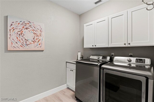 clothes washing area with washer and clothes dryer, cabinets, and light wood-type flooring