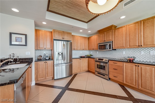 kitchen with decorative backsplash, stainless steel appliances, a raised ceiling, sink, and dark stone countertops