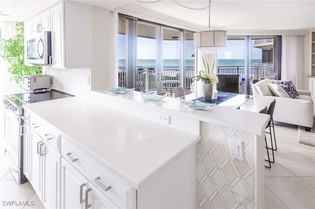 kitchen featuring kitchen peninsula, expansive windows, stainless steel appliances, a water view, and white cabinetry