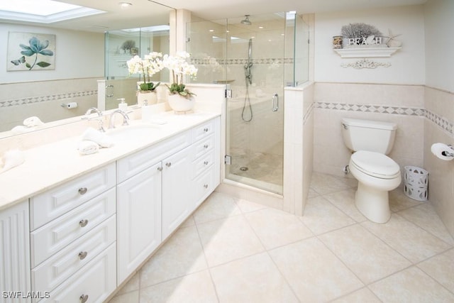 bathroom with tile patterned flooring, toilet, vanity, a shower with shower door, and tile walls