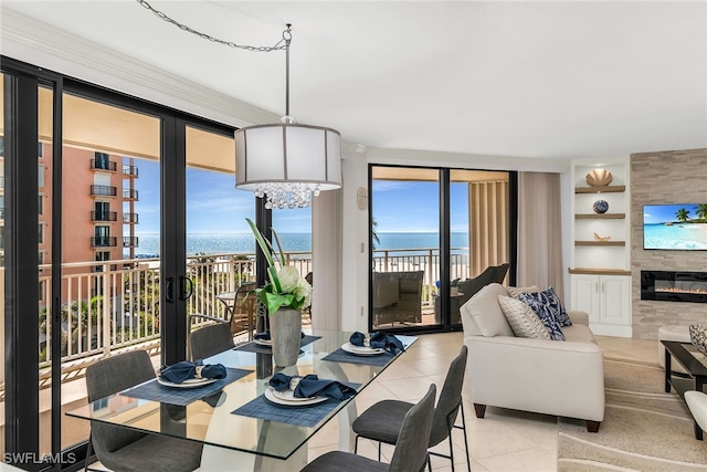 dining area featuring built in shelves, a water view, a tile fireplace, light tile patterned flooring, and a notable chandelier