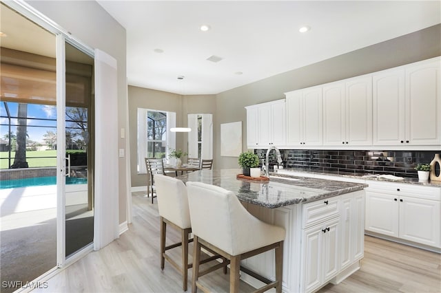 kitchen featuring tasteful backsplash, a kitchen island with sink, sink, stone counters, and white cabinets