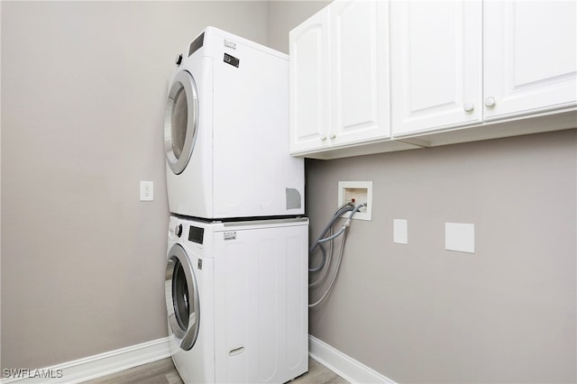 laundry area featuring cabinets, light wood-type flooring, and stacked washer / dryer