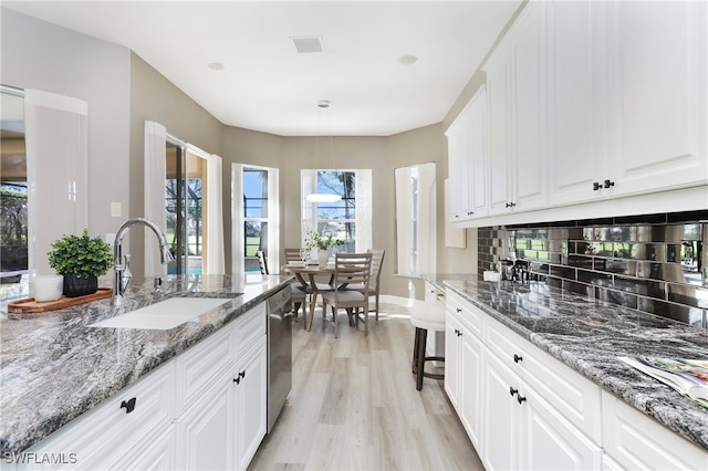 kitchen with light wood-type flooring, white cabinetry, dark stone counters, and sink