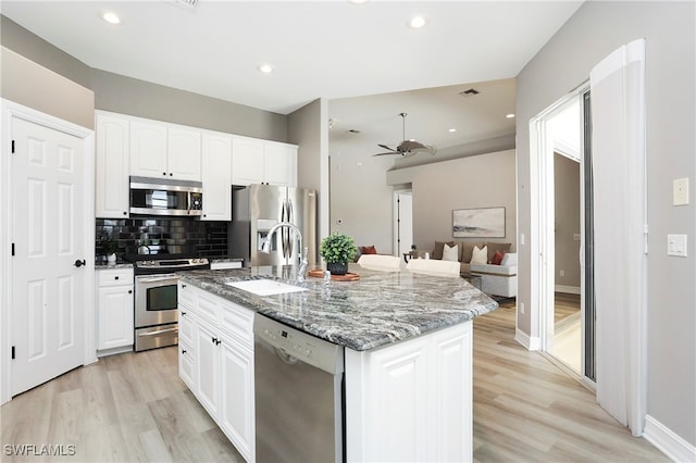 kitchen featuring appliances with stainless steel finishes, a kitchen island with sink, sink, white cabinets, and light hardwood / wood-style floors