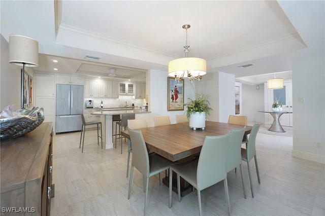 dining room with a tray ceiling, sink, a chandelier, and ornamental molding