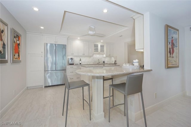 kitchen featuring stainless steel built in refrigerator, backsplash, ceiling fan, light stone countertops, and white cabinetry