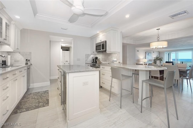 kitchen with light stone countertops, backsplash, stainless steel appliances, a center island, and white cabinetry