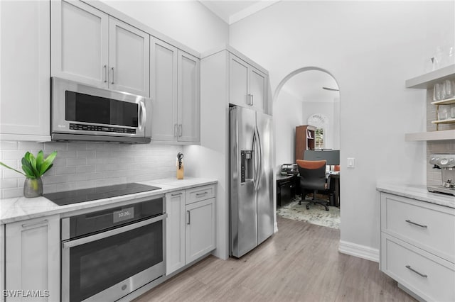 kitchen with light stone countertops, appliances with stainless steel finishes, light wood-type flooring, and tasteful backsplash