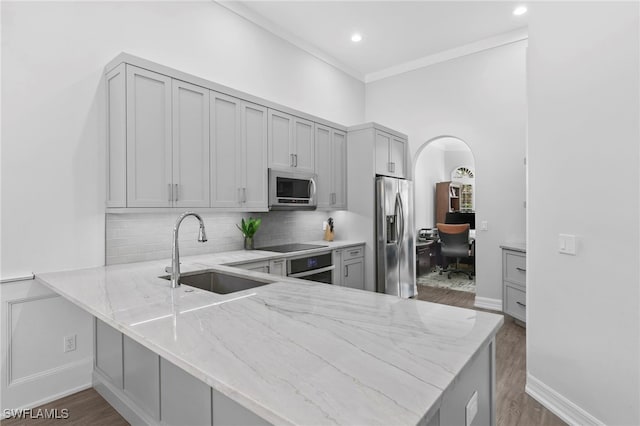 kitchen with appliances with stainless steel finishes, sink, kitchen peninsula, light stone counters, and gray cabinetry