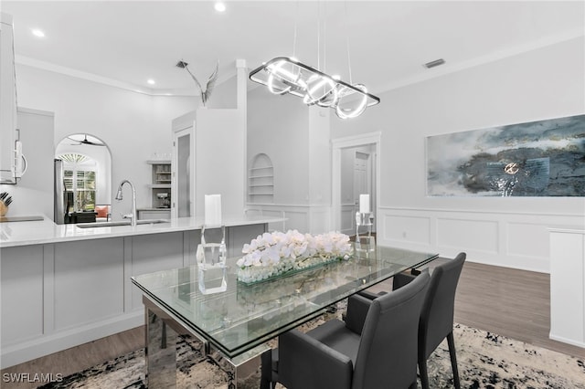 dining space with wood-type flooring, built in features, a notable chandelier, and ornamental molding