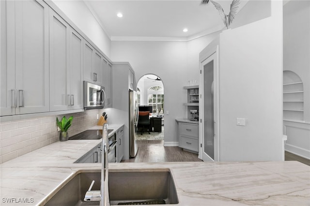 kitchen featuring tasteful backsplash, gray cabinetry, hardwood / wood-style floors, ornamental molding, and stainless steel appliances