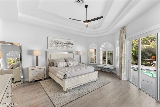 bedroom featuring access to exterior, light hardwood / wood-style flooring, ceiling fan, and a raised ceiling