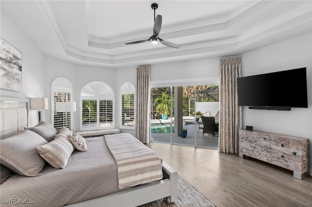 bedroom featuring ceiling fan, hardwood / wood-style floors, access to exterior, and a tray ceiling