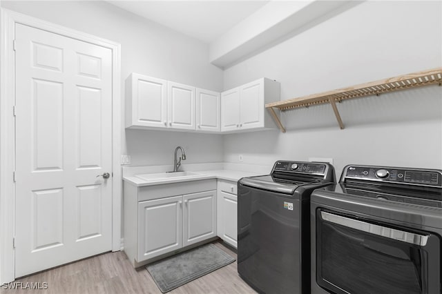 laundry room with light hardwood / wood-style floors, sink, washer and clothes dryer, and cabinets