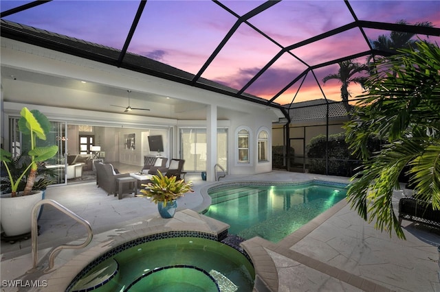 pool at dusk featuring glass enclosure, ceiling fan, an in ground hot tub, outdoor lounge area, and a patio area