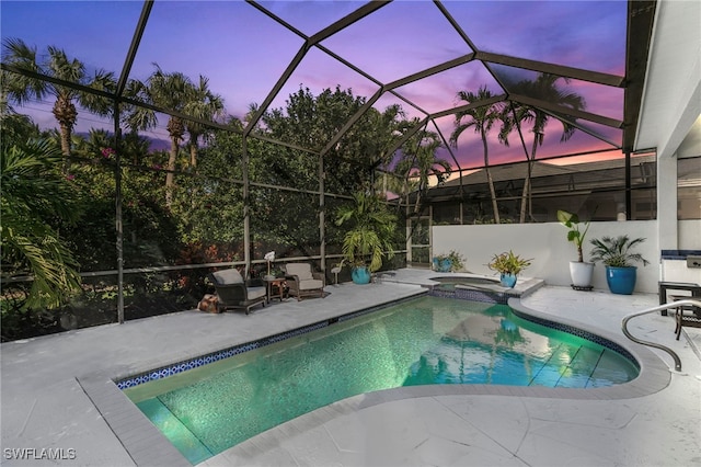 pool at dusk featuring a patio, an in ground hot tub, and glass enclosure